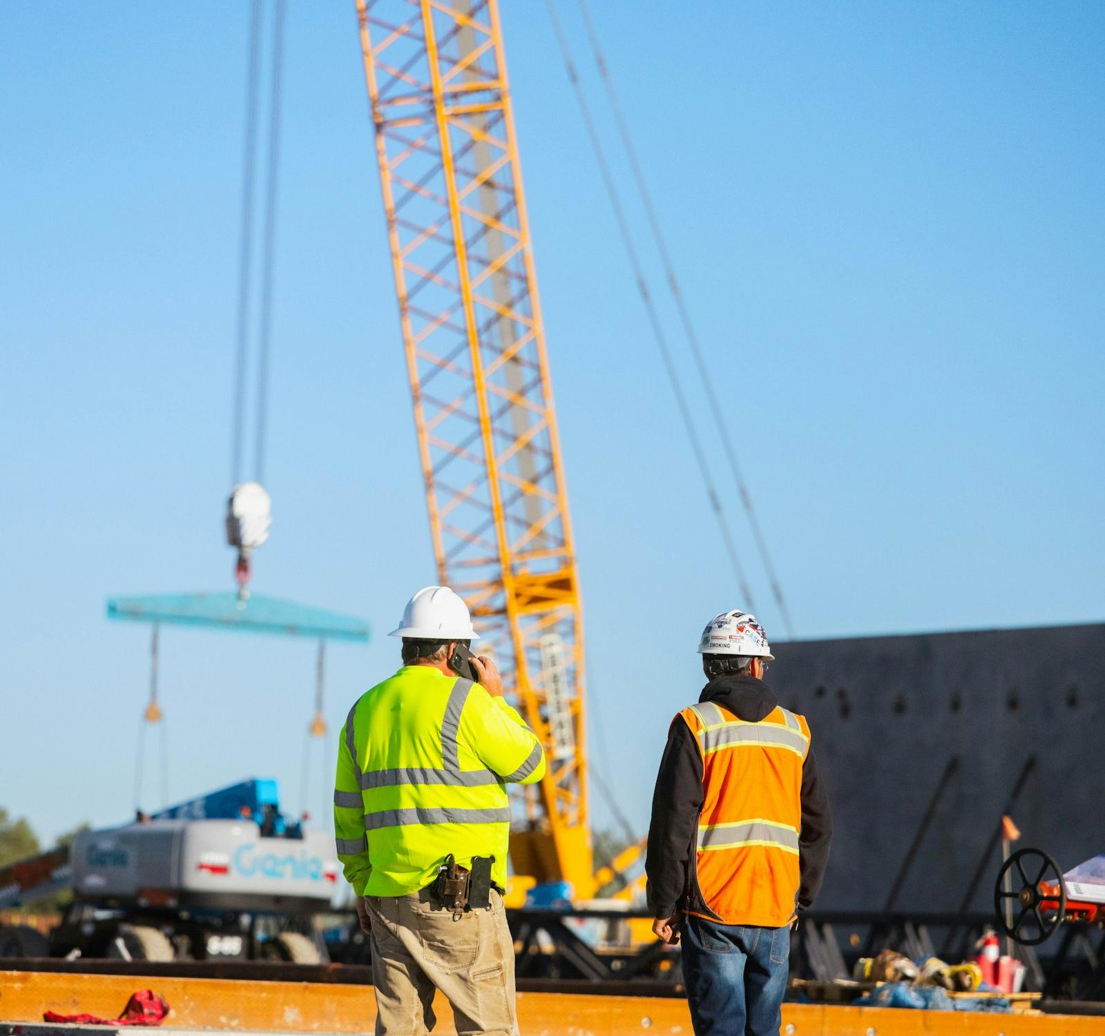 Construction crew in high-visibility vests watching a crane set a precast panel on a commercial job site